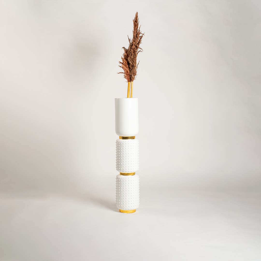White ceramic and gold stacked vase displayed in a bright minimal setting with soft shadows highlighting its textured design and tall vertical form.