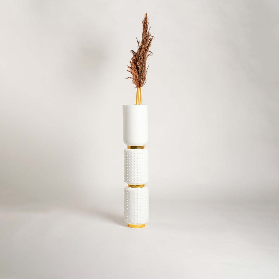 White ceramic and gold stacked vase displayed in a bright minimal setting with soft shadows highlighting its textured design and tall vertical form.