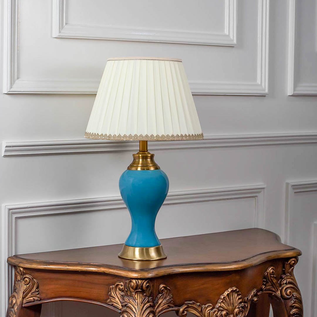 Blue ceramic table lamp turned off with pleated shade and golden base displayed on minimal white background.