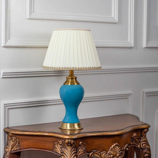 Blue ceramic table lamp turned off with pleated shade and golden base displayed on minimal white background.