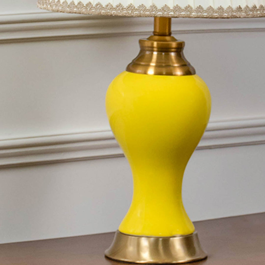 Closeup of yellow ceramic table lamp with glossy ceramic finish brass detailing and pleated fabric shade.