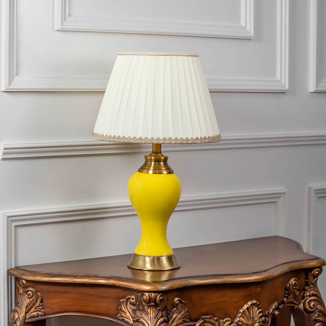 Yellow ceramic table lamp with classic fabric shade placed on wooden table adding warm and cheerful home lighting accent.