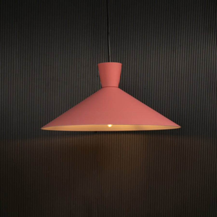 Pink cone pendant light hanging against dark textured wall with light on for playful modern décor.