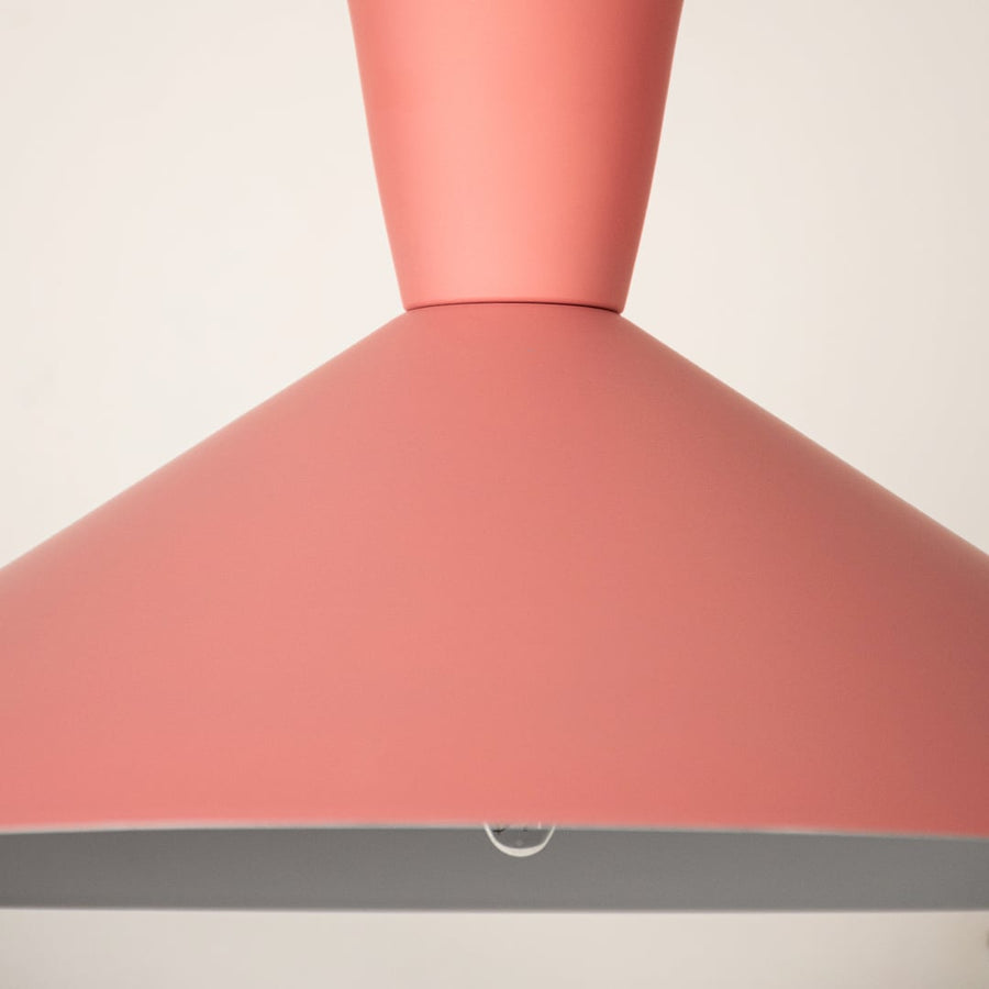 Pink cone pendant light shown in close up view against soft white background with light off for playful modern décor.