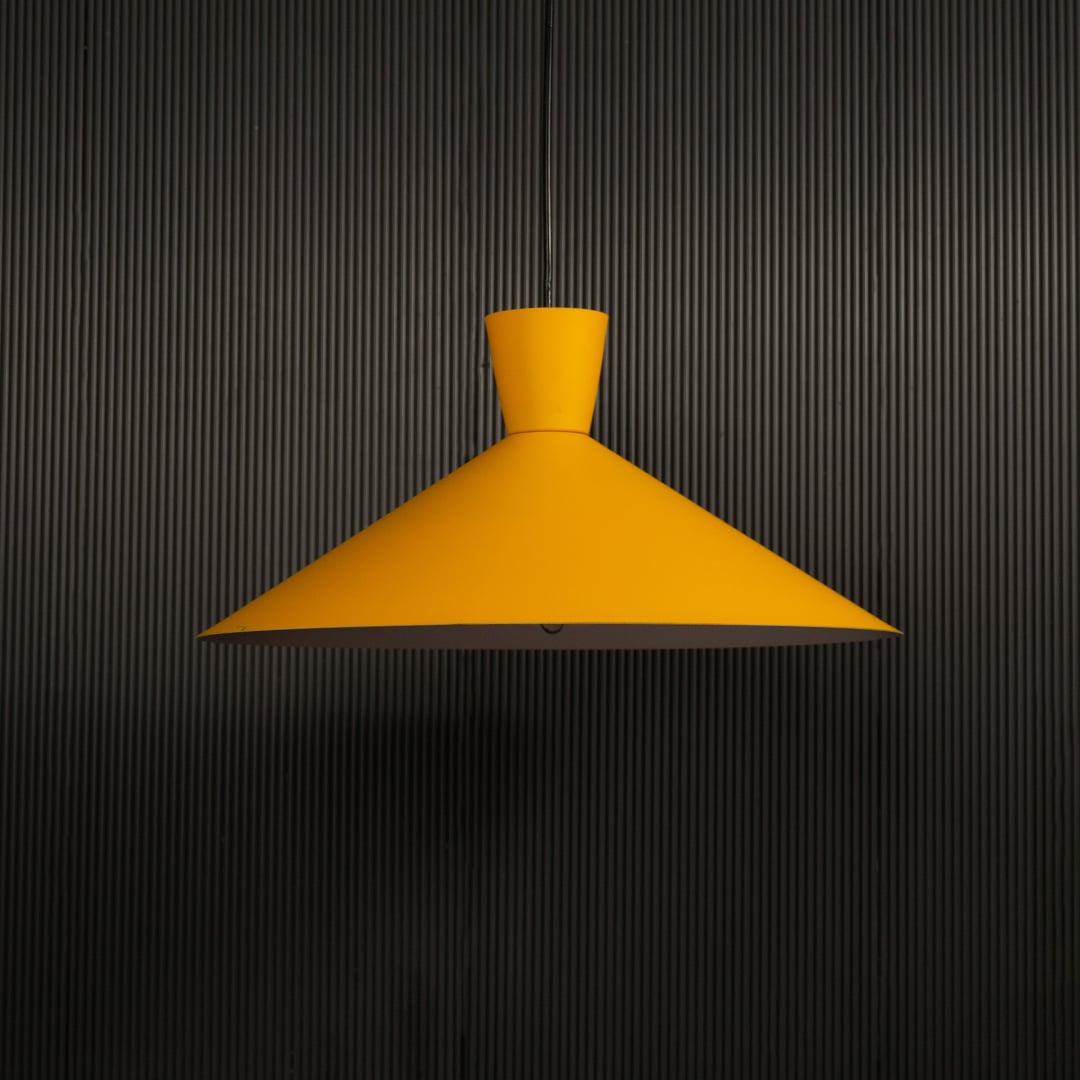 Yellow cone pendant light hanging against dark textured wall with light on for bright modern décor.