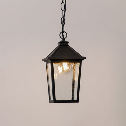 Black outdoor lantern with the light switched on displayed on a white background showing a warm glow through textured clear glass.