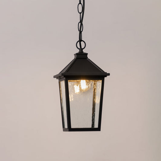 Black outdoor lantern with the light switched on displayed on a white background showing a warm glow through textured clear glass.