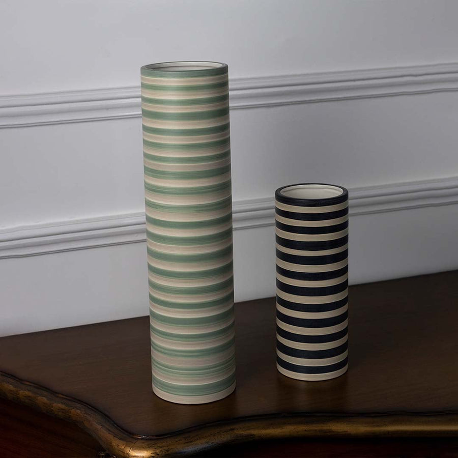 Striped ceramic vase in tall cylindrical shape shown as part of a grouped display with a clean minimal white backdrop.