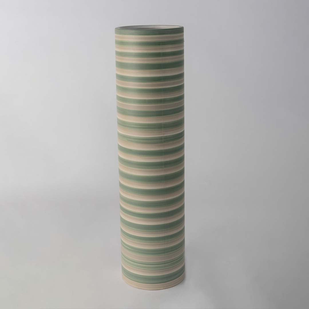 Tall striped ceramic vase in green and beige tones standing on a clean white background highlighting its smooth modern cylindrical shape.