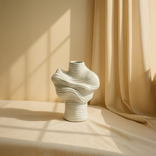 White ceramic sculptural vase with artistic folded design placed on beige surface for modern minimal home decor.