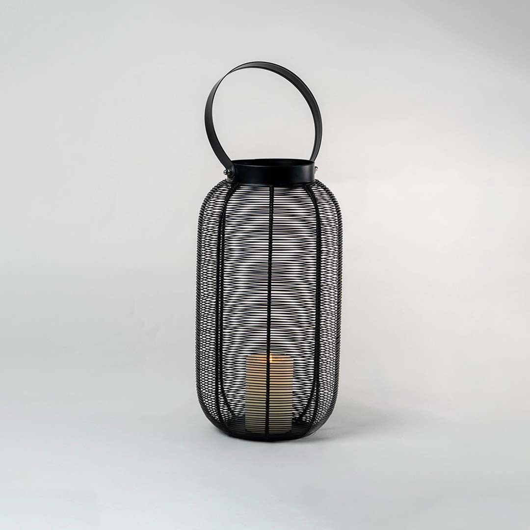 Illuminated black metal wire lantern isolated on white background showing warm candle glow casting shadows through mesh design.