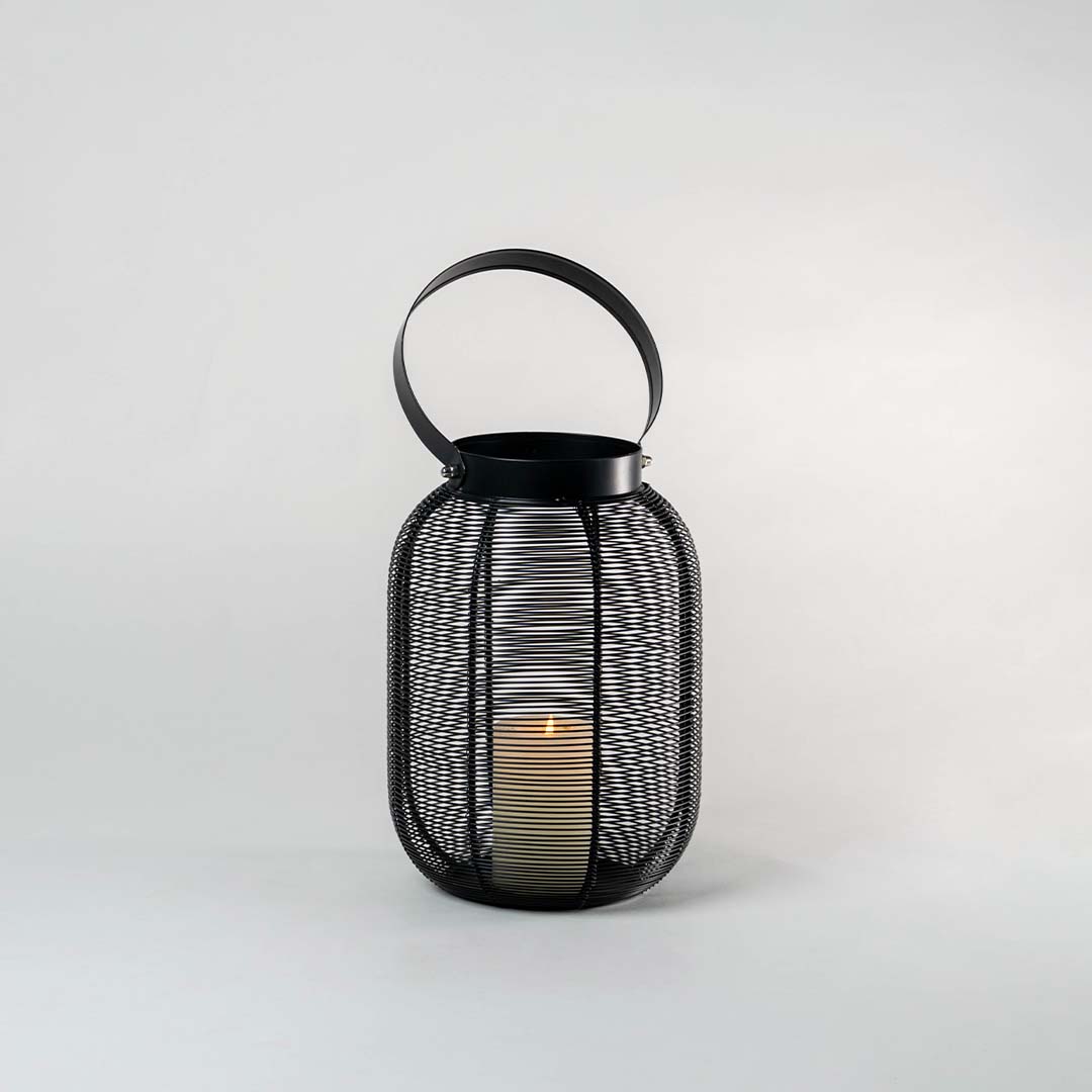 Illuminated copper wire lantern isolated on white background showing warm LED candle light glow casting shadows through metal mesh frame.