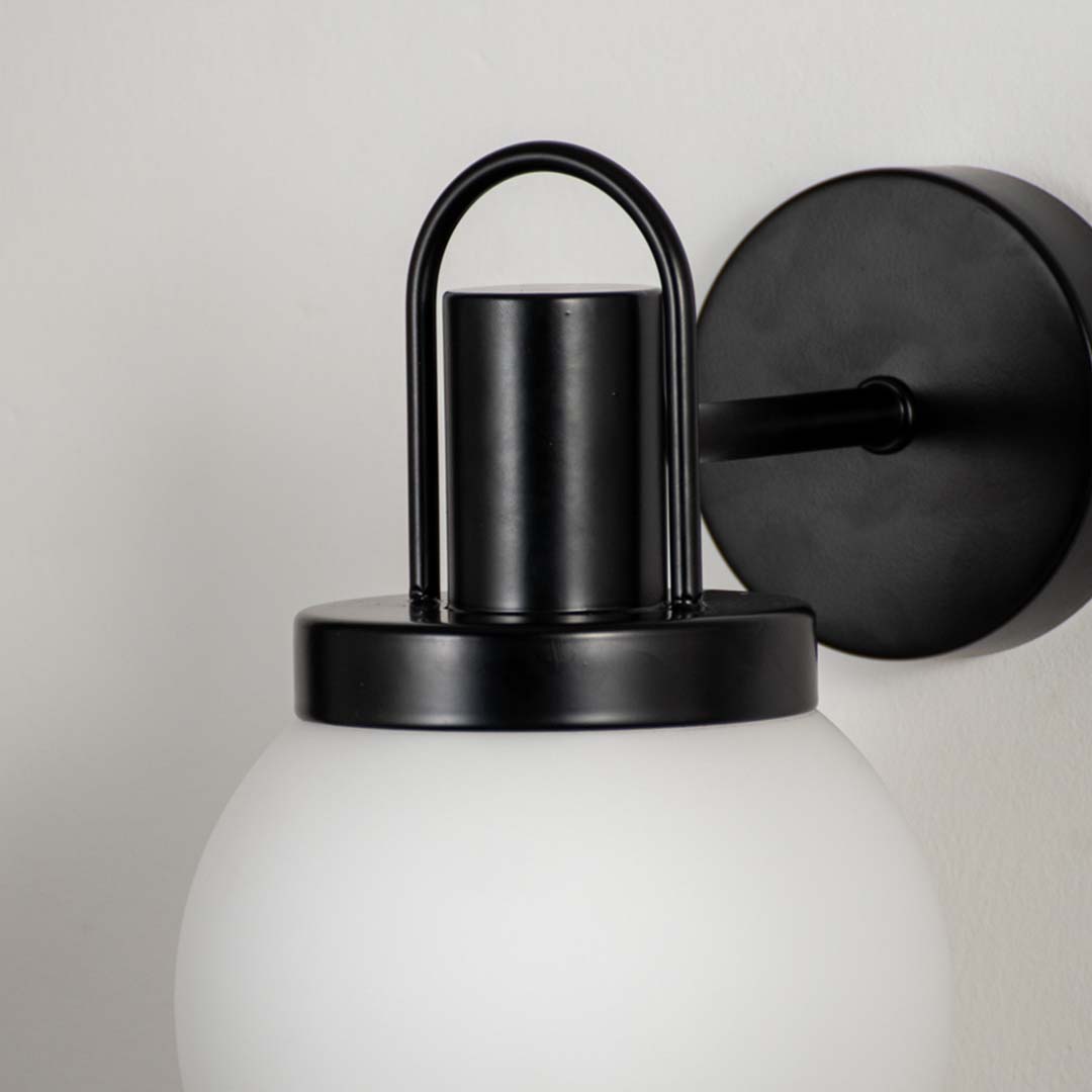 Closeup of frosted glass globe wall lamp with black metal fixture showing modern style details for living room wall lighting.