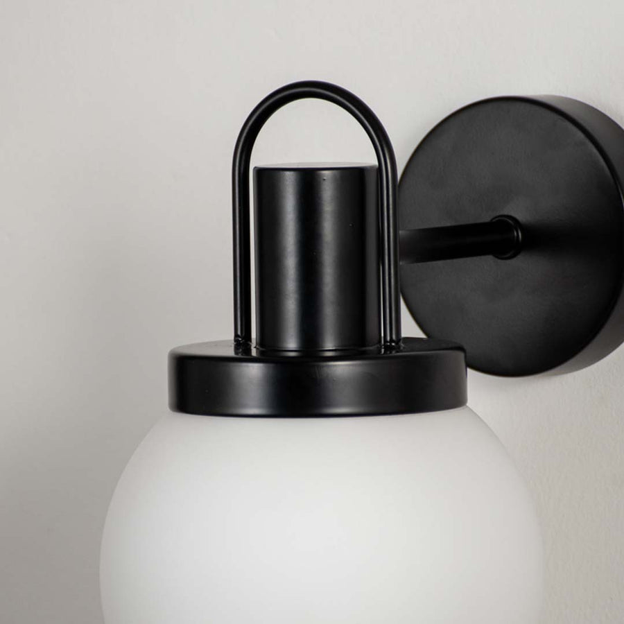Closeup of frosted glass globe wall lamp with black metal fixture showing modern style details for living room wall lighting.