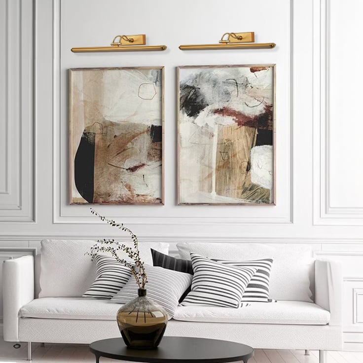 Gold adjustable picture light mounted above artwork creating warm focused illumination for elegant living room and hallway decor.
