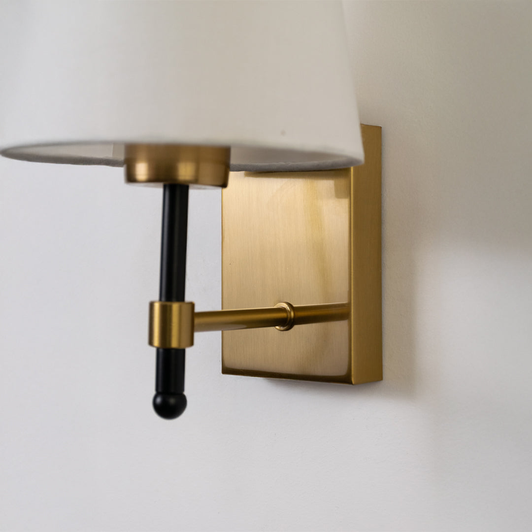 Closeup wall light in gold metal finish with fabric shade for bedroom or living room decor lighting white background.