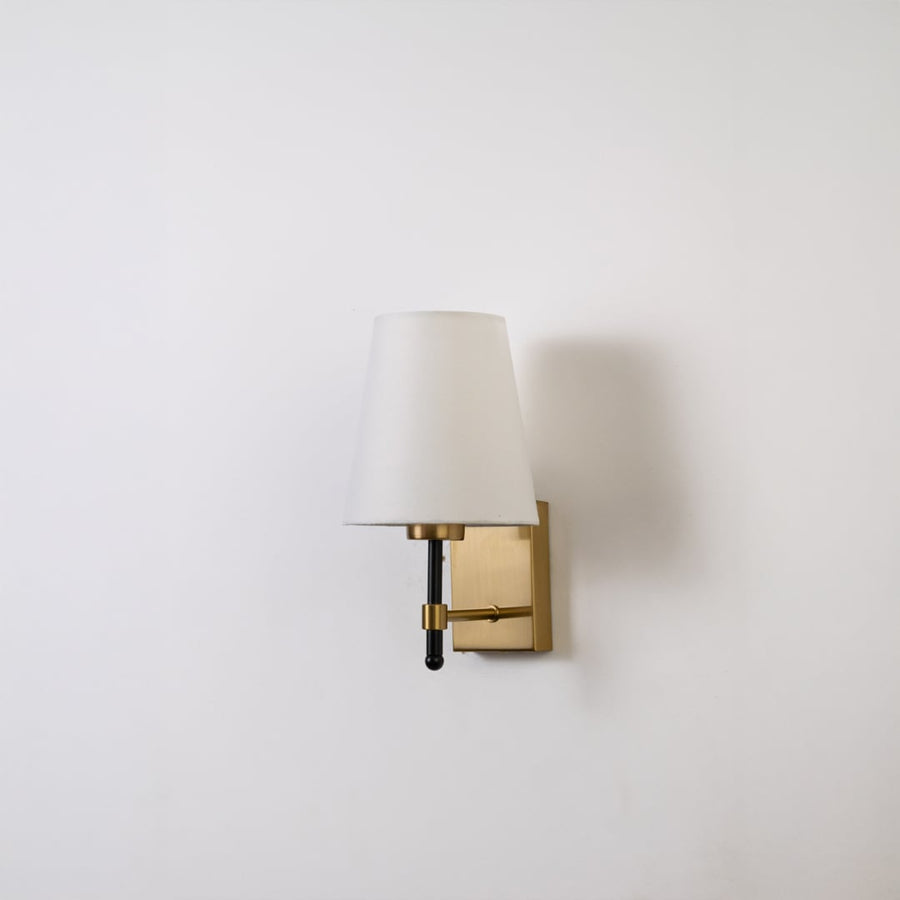 Gold metal wall light with white fabric shade displayed on a white background with light off highlighting its sleek modern shape.