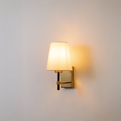 Gold metal wall light with white fabric shade glowing softly on a clean white background ideal for bedroom hallway and living room wall lighting.