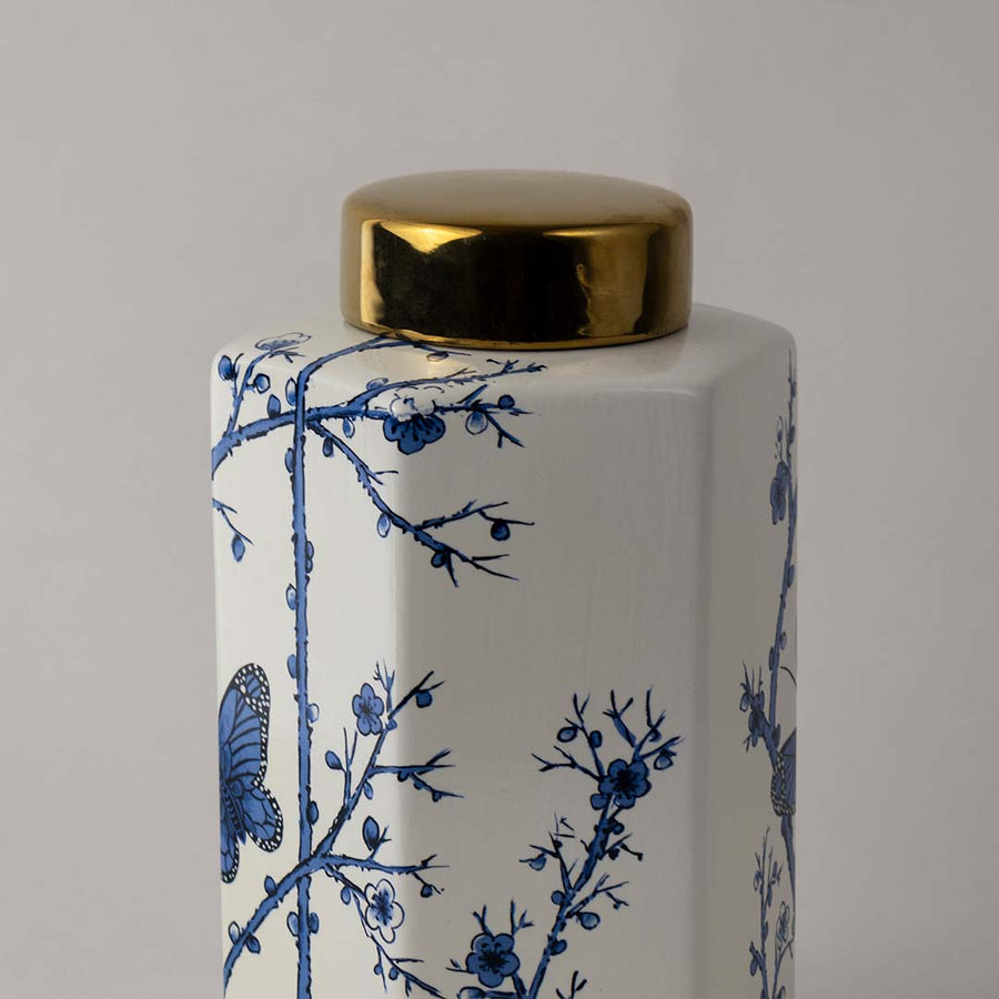 Closeup of ceramic decor jar showing fine blue floral detailing and butterfly art with shiny gold lid finish.