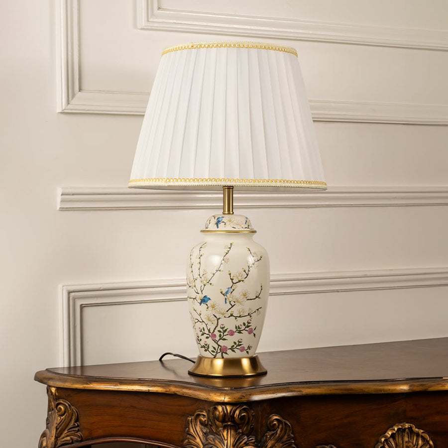 Ceramic floral table lamp with white shade displayed on white wall background lights turned off.