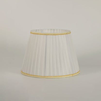 Elegant pleated white lampshade with golden lace trim styled in modern interior for soft ambient lighting.