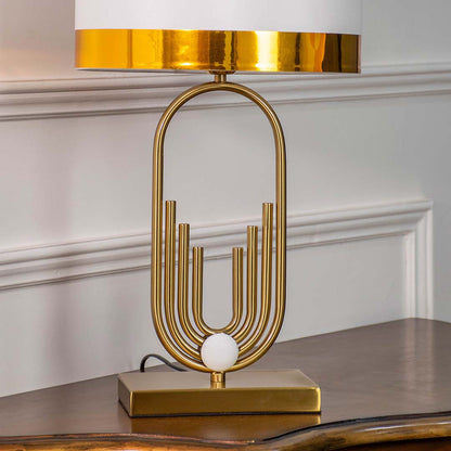 Gold sculptural table lamp with white shade on wooden console table with light off and white panel wall for artistic modern décor.