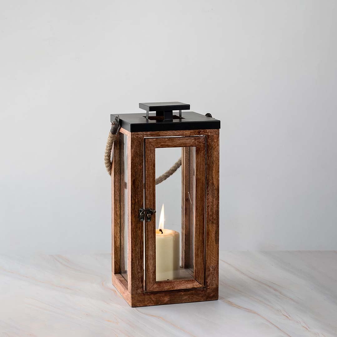Tall wooden lantern turned on displayed on white background highlighting rustic wood and glass design.