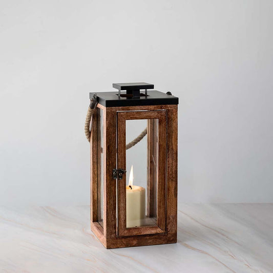 Tall wooden lantern turned on displayed on white background highlighting rustic wood and glass design.
