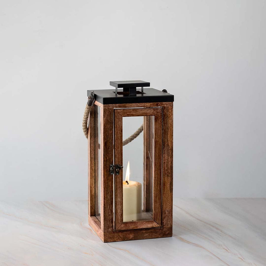 Tall wooden lantern turned on displayed on white background highlighting rustic wood and glass design.