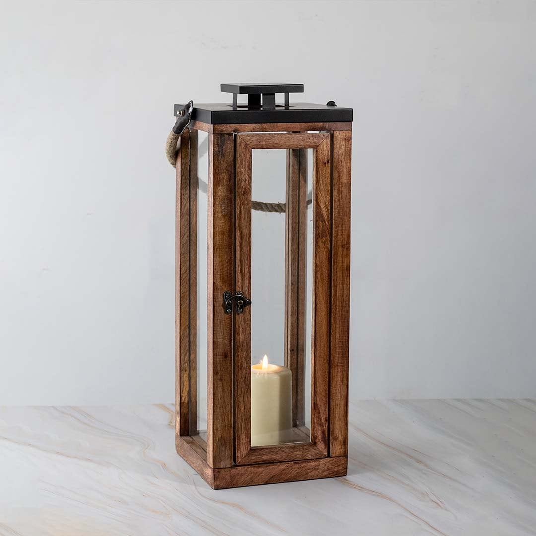 Tall wooden lantern turned on displayed on white background highlighting glass and wood finish.