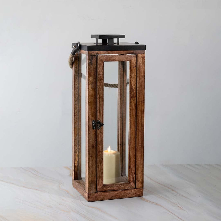 Tall wooden lantern turned on displayed on white background highlighting glass and wood finish.