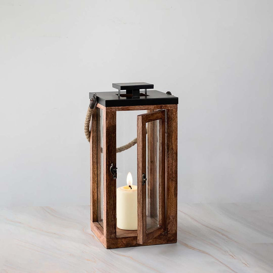 Tall wooden lantern with glass panels and candle lit displayed on white background for home accents.