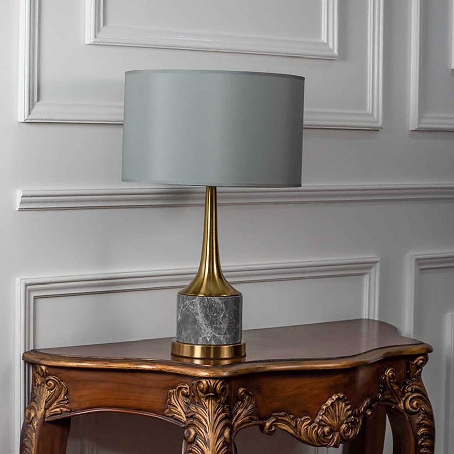 Grey shade gold neck table lamp on carved console table with light off and white panel wall background for luxury contemporary décor.