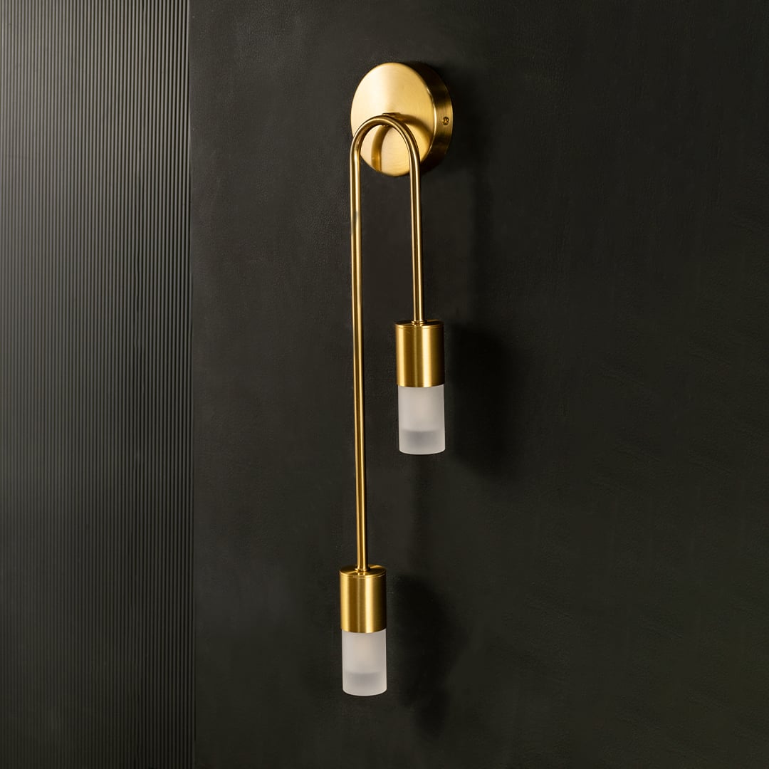 A modern dual gold metal wall lamp with frosted glass shades shown with lights off against a dark background emphasizing its sleek minimal silhouette.