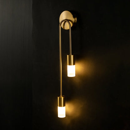 A glowing dual gold wall light with frosted glass shades illuminated against a dark background creating a dramatic elegant and modern lighting effect.