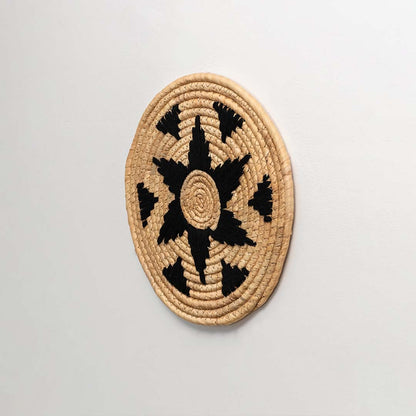 Side profile of the flat woven wall basket showing the thick natural fiber coils and black wrapping details on a white surface.
