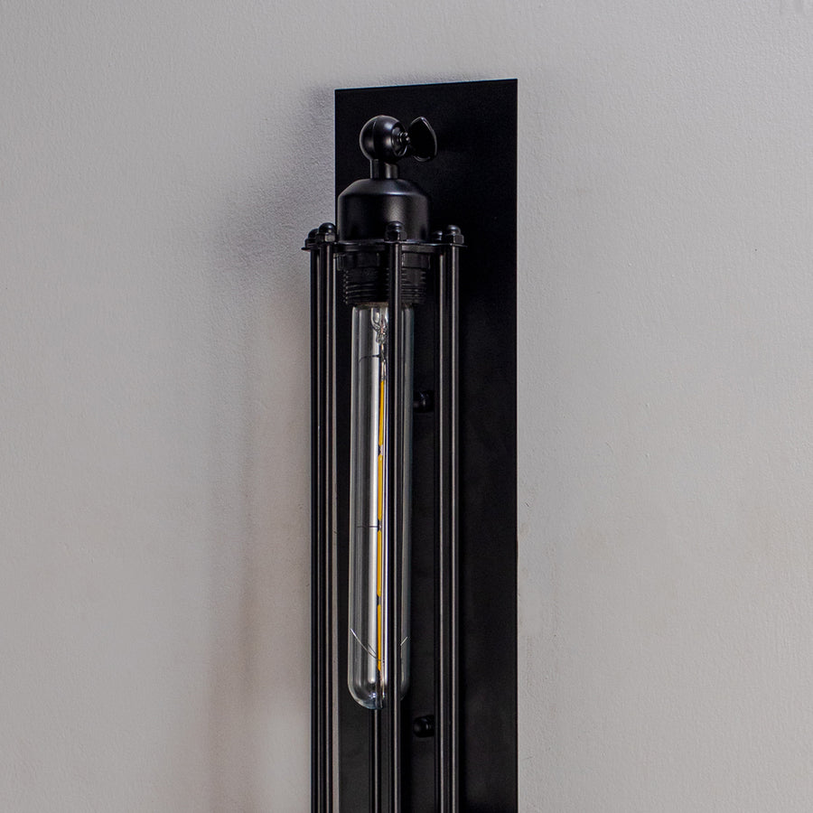Close up wall light with black metal finish and tubular bulb on dark background modern industrial lighting for home decor.