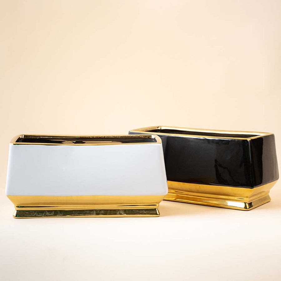 Set of two rectangular ceramic vases in contrasting black and white colors with gold bases and rims arranged together on a beige background showcasing sophisticated decor pairing.