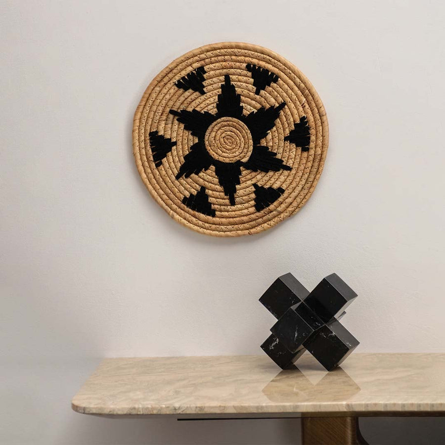 Natural seagrass wall plate with black star design arranged on a plain wall above a wooden table for minimalist bohemian styling.