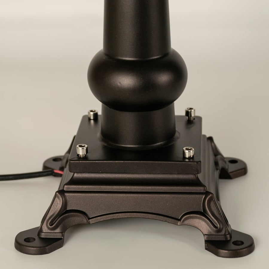 Closeup of a black outdoor pillar lamp showing glowing frosted glass and refined lantern edges designed for soft ambient garden and pathway lighting.