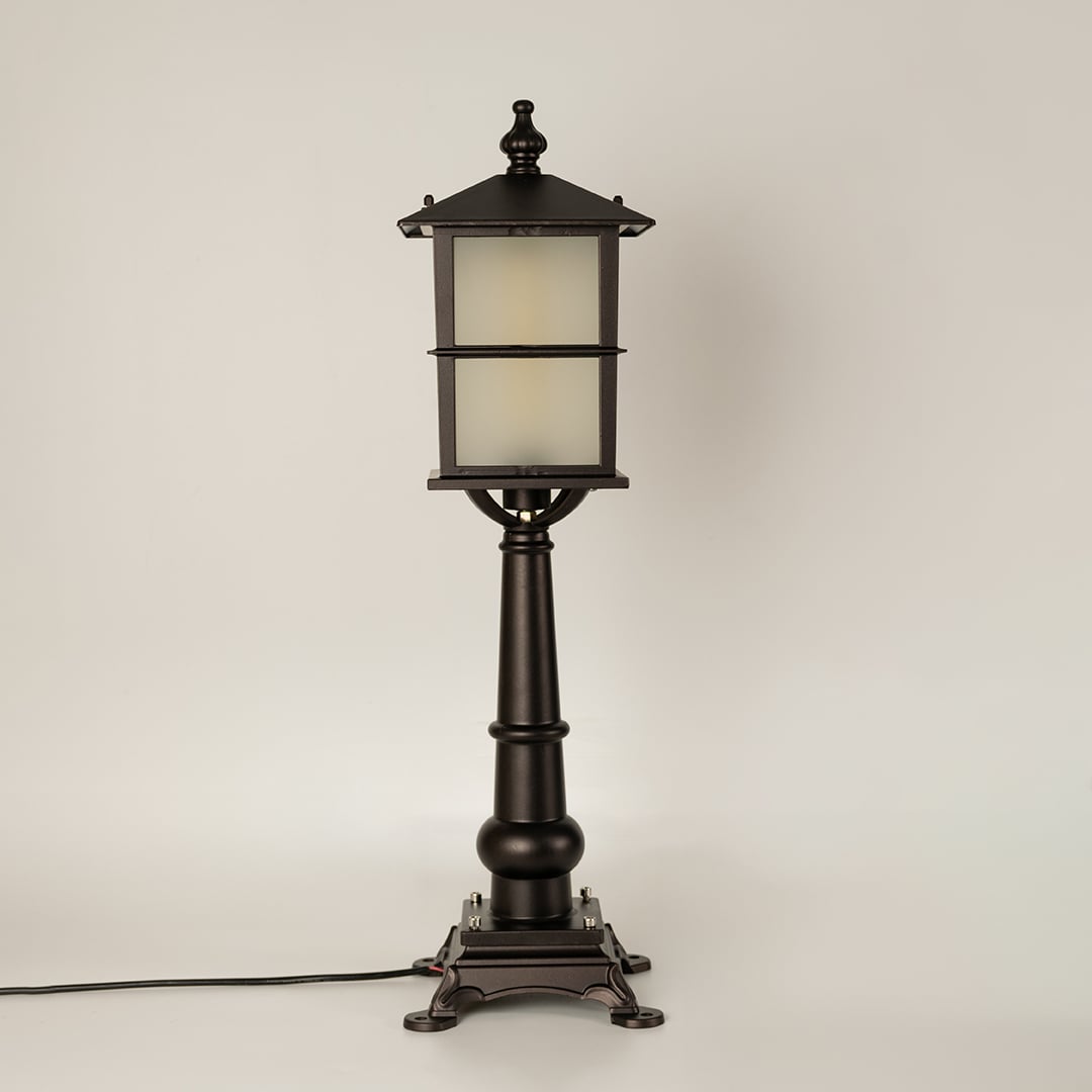 A black outdoor pillar lamp with frosted glass shown with light off on a white background emphasizing its clean lantern frame and ornate pillar detailing.