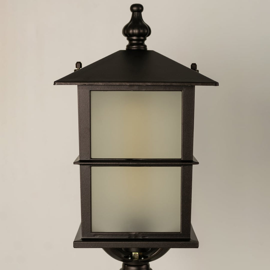 Closeup of a black outdoor pillar lamp showing glowing frosted glass and refined lantern edges designed for soft ambient garden and pathway lighting.