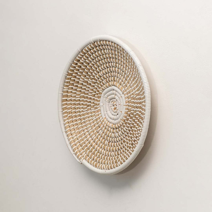 A side angle of a beige and white wicker wall decor plate highlighting its raised woven structure and handcrafted natural fiber detailing.