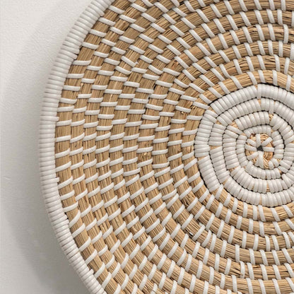 A closeup of a beige and white wicker wall plate showing its spiral weave pattern and textured natural fibers for detailed decor viewing.