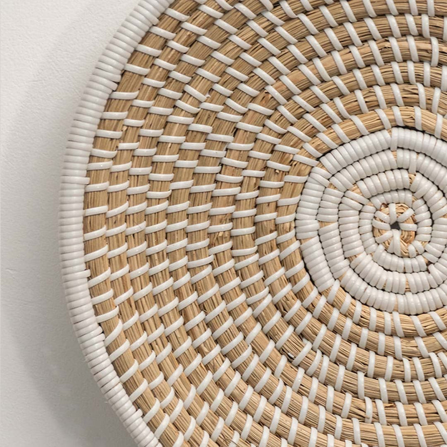 A closeup of a beige and white wicker wall plate showing its spiral weave pattern and textured natural fibers for detailed decor viewing.