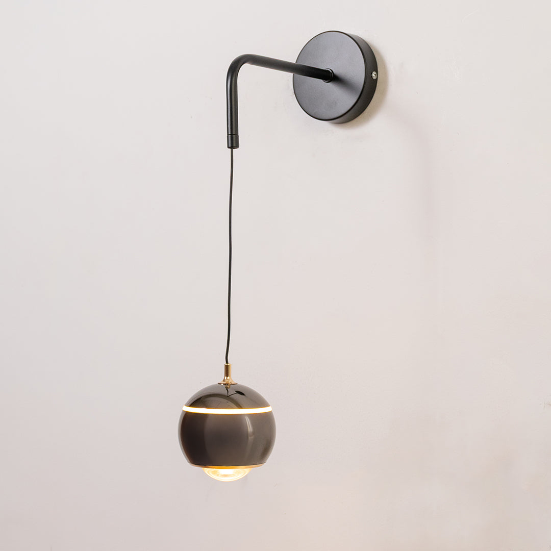Modern wall light in black metal finish with hanging globe shade for bedroom or living decor lighting white background.