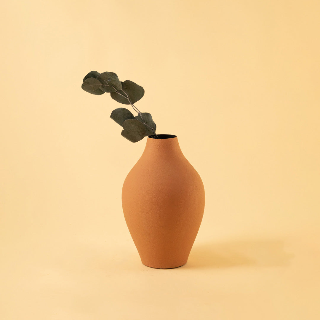 Elegant matte orange metal bud vase with greenery stem for minimalist home decor and cozy tabletop aesthetics.