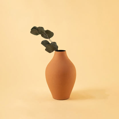 Elegant matte orange metal bud vase with greenery stem for minimalist home decor and cozy tabletop aesthetics.