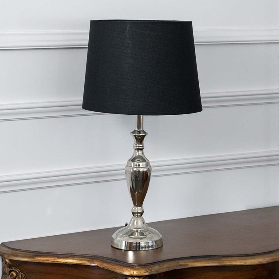 Black fabric shade table lamp with brass base glowing softly on a classic wooden side table adding a cozy ambiance.