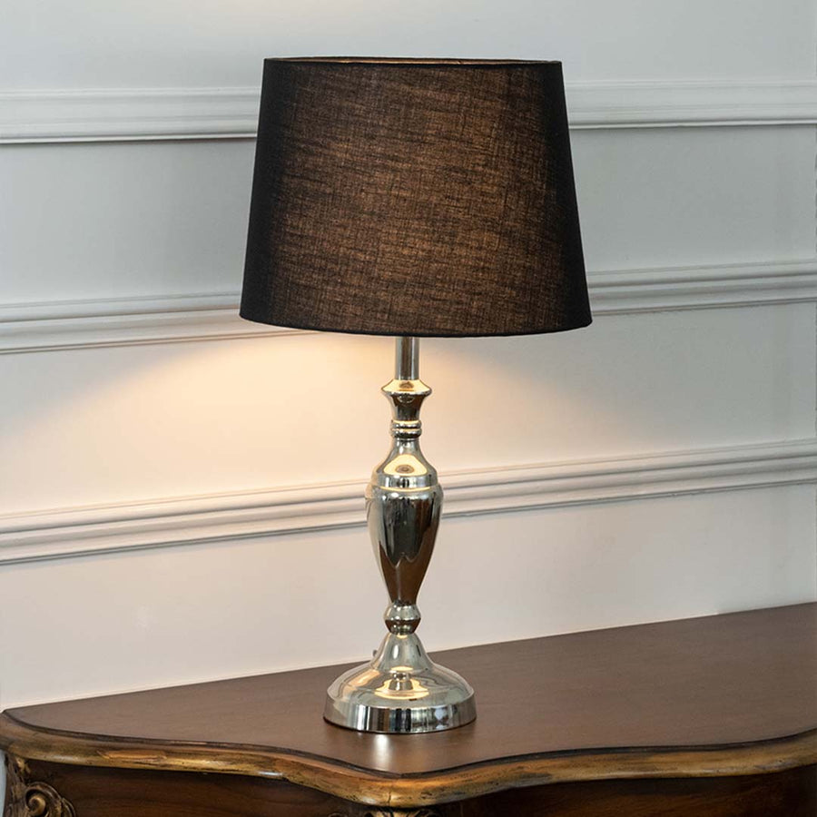 Silver glass table lamp with black fabric shade offering elegant contemporary decor and warm ambient lighting indoors.